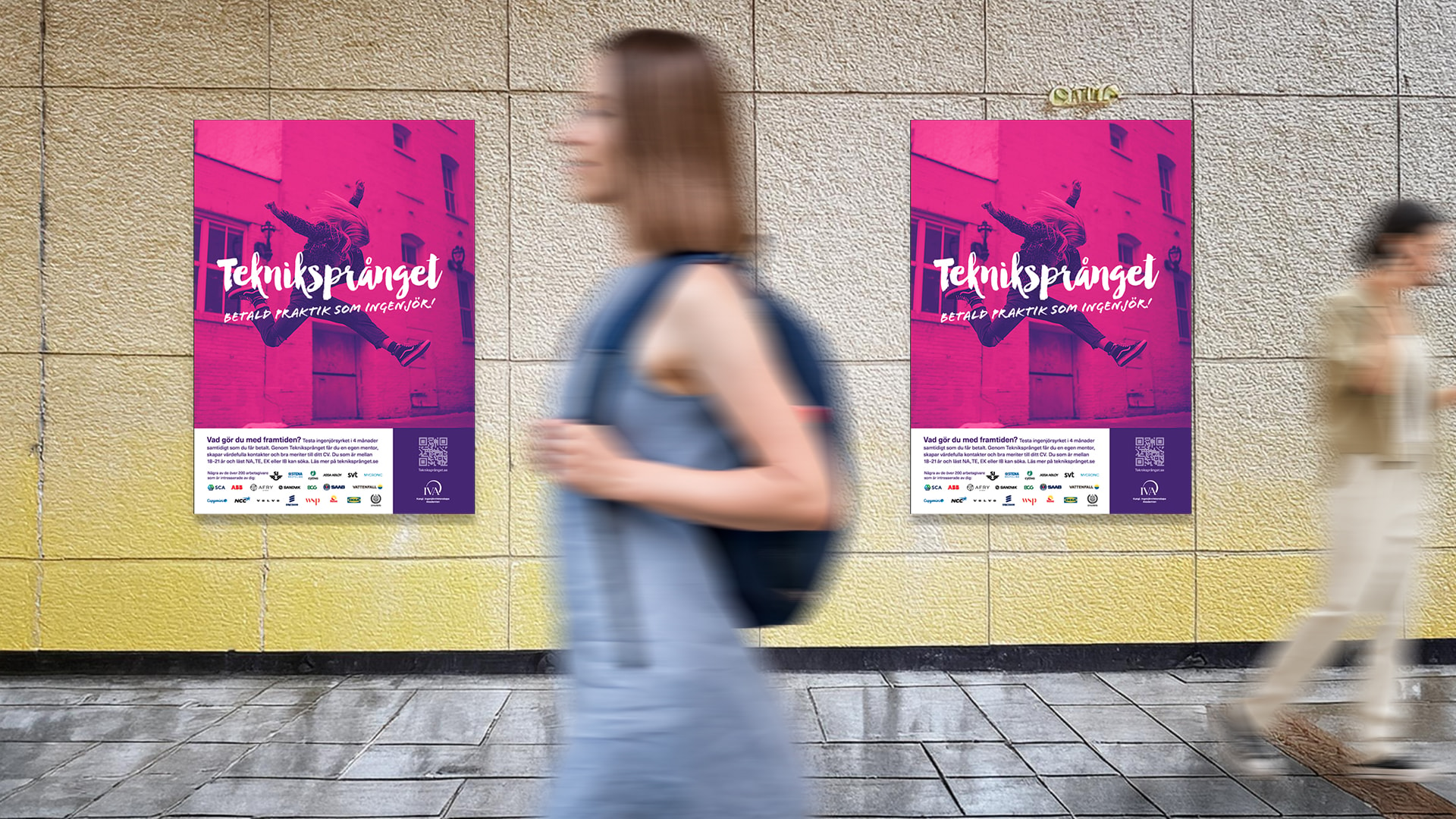 Två personer går i en korridor där två posters med Tekniksprångetinformation hänger på väggen