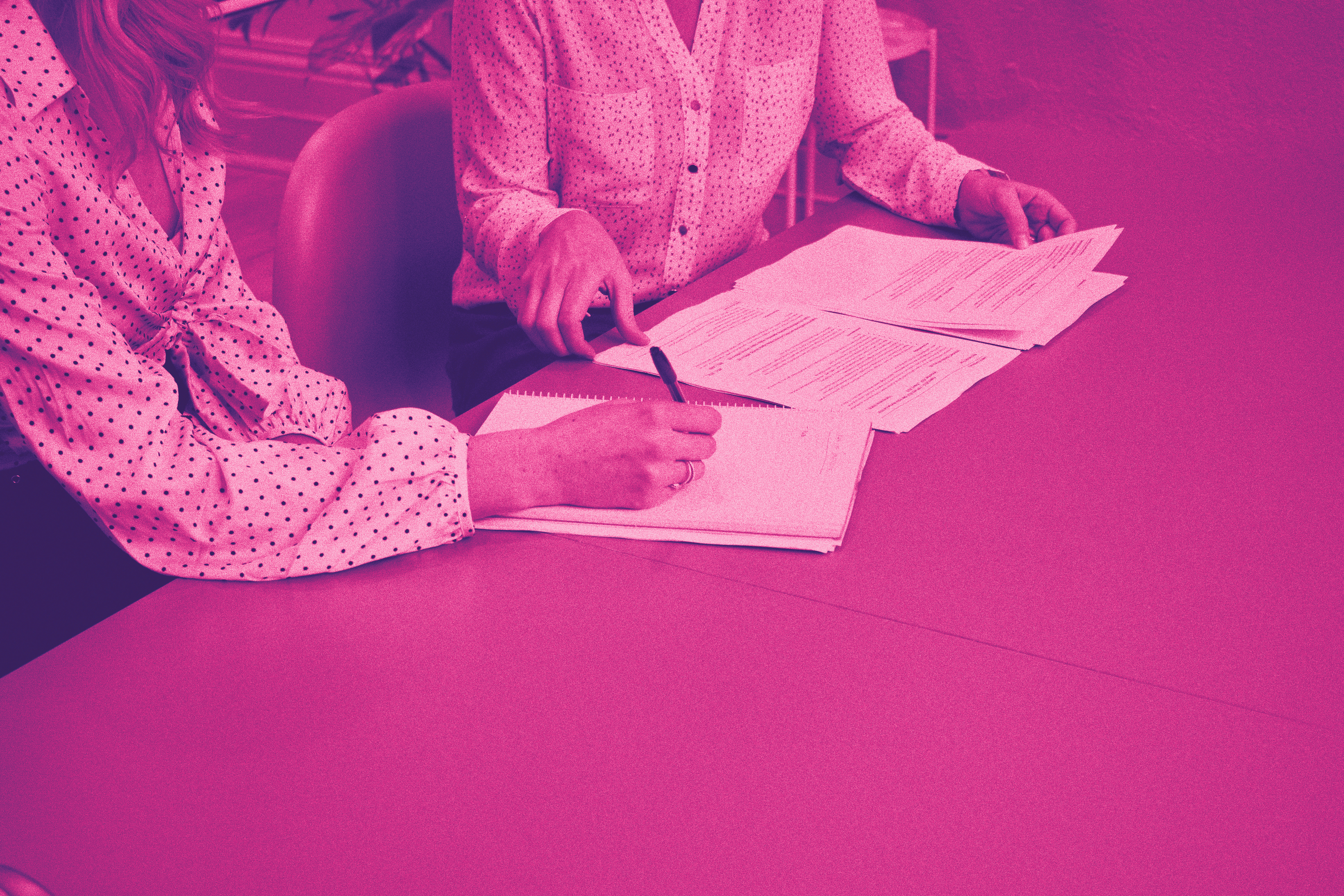 Two women sit at a table and sign contracts. With pink filter