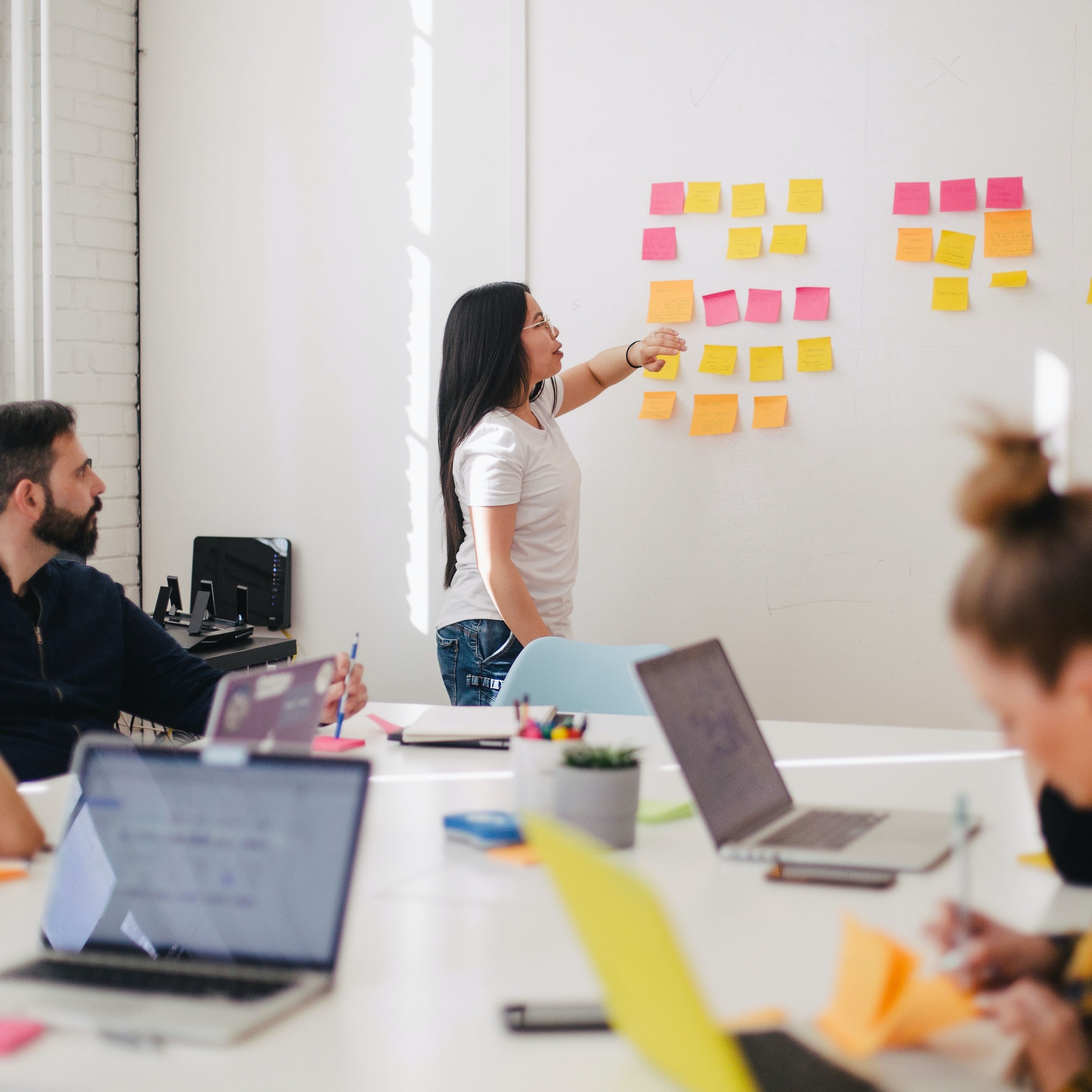 Kvinna vid whiteboard täckt i postitlappar presenterar för en grupp personer 