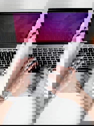 Bild ovanifrån där person arbetar på laptop. Allt vi ser är två händer och datorn.