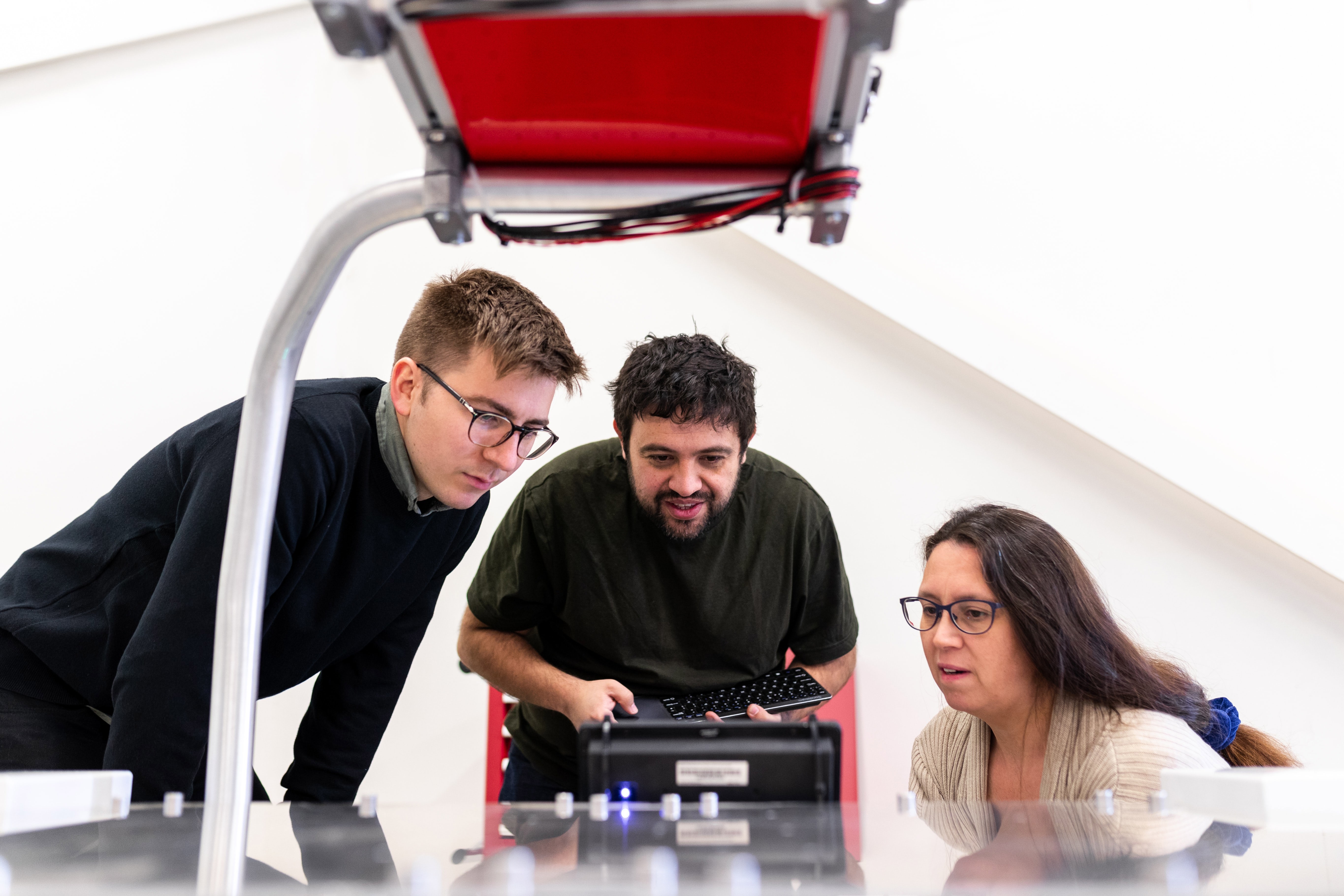 Three people look at a small machine.